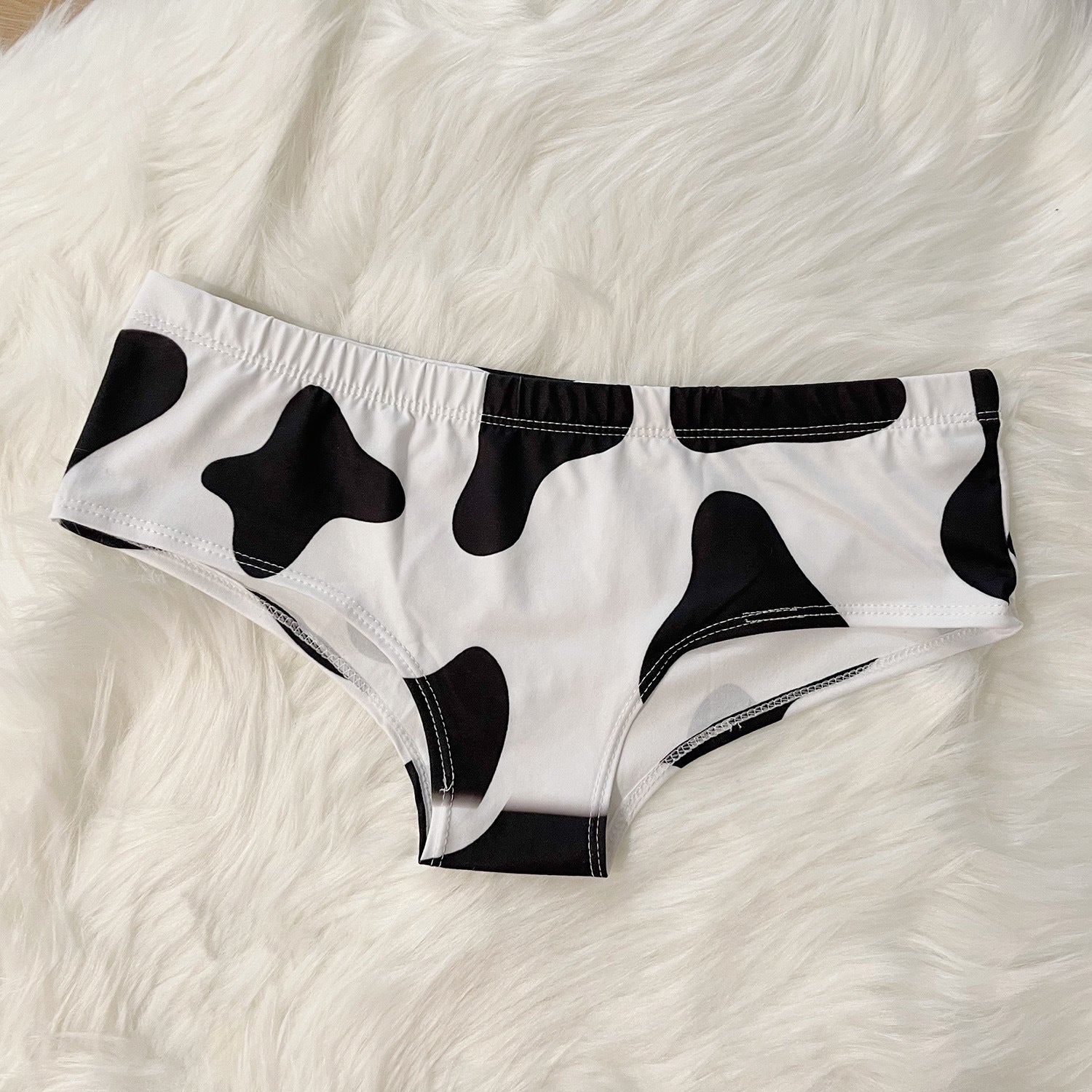 Black and white cow print femboy underwear flatlay, soft novelty panties product shot
