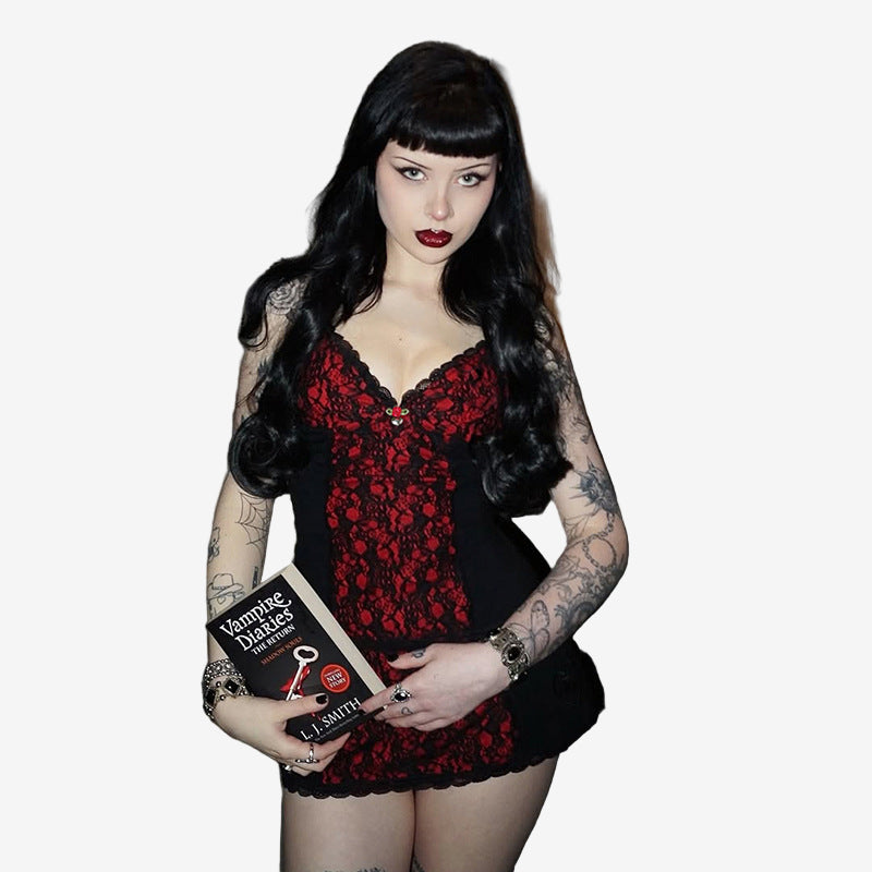low-angle medium shot of a model cradling a horror paperback at waist level, highlighting the red lace front panel and slim fit of the cami against a moody grey backdrop, ideal for femboy outfits.