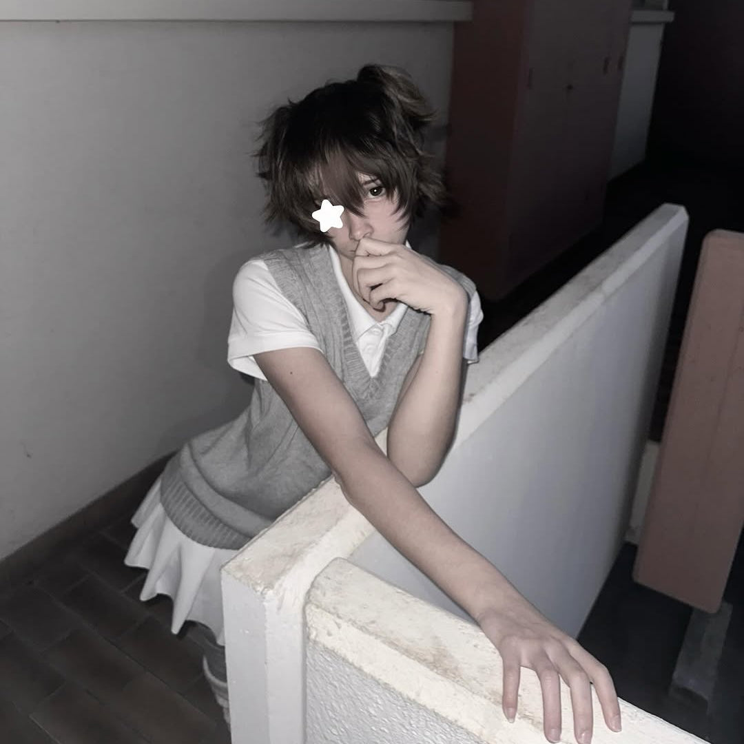 Femboy in grey sweater vest and white pleated skirt college outfit, cute seated lifestyle shot