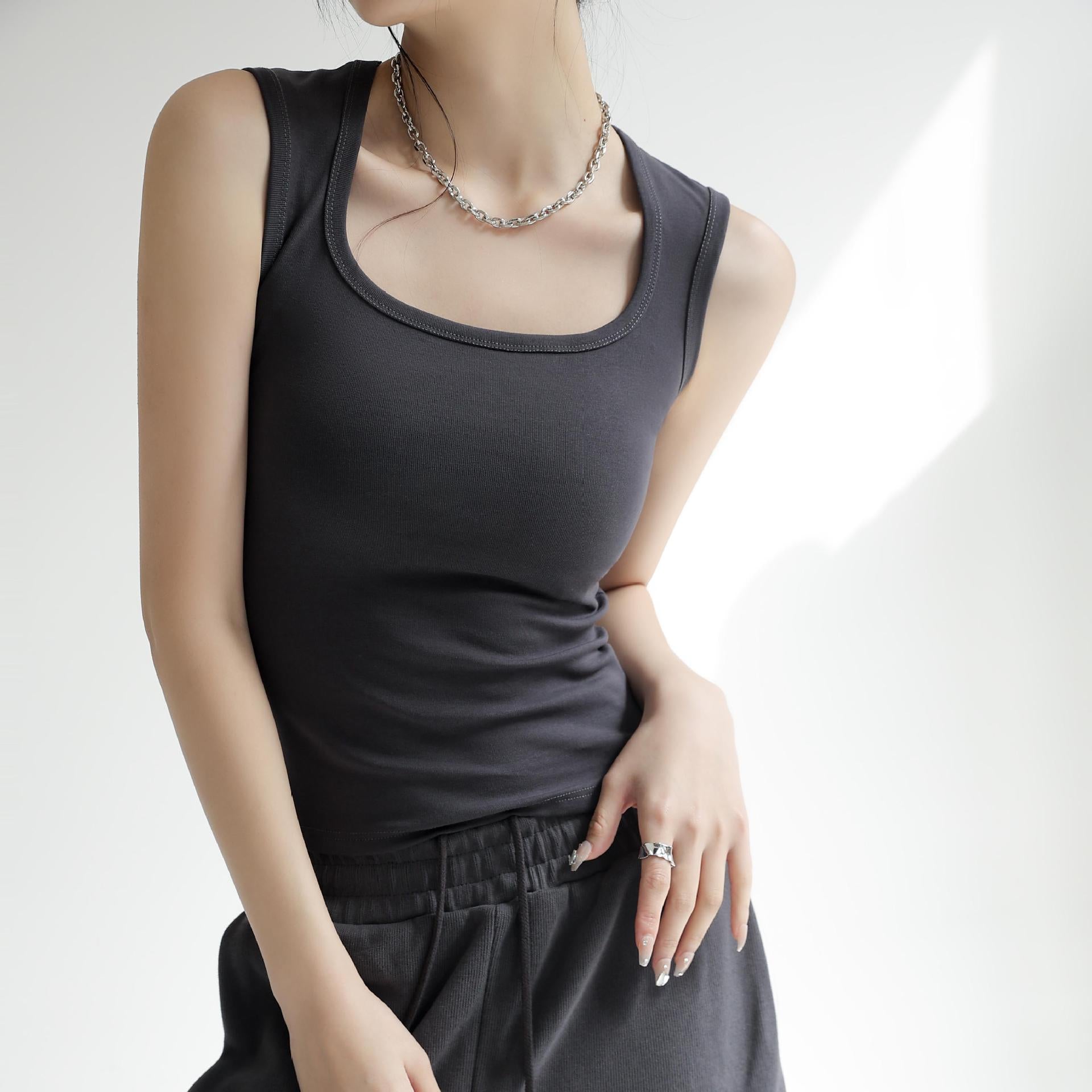Three-quarter torso shot of an androgynous femboy model wearing a charcoal grey fitted cotton tank top, emphasizing clean lines, smooth texture and everyday wearability, captured in a minimal studio setting with soft natural lighting.