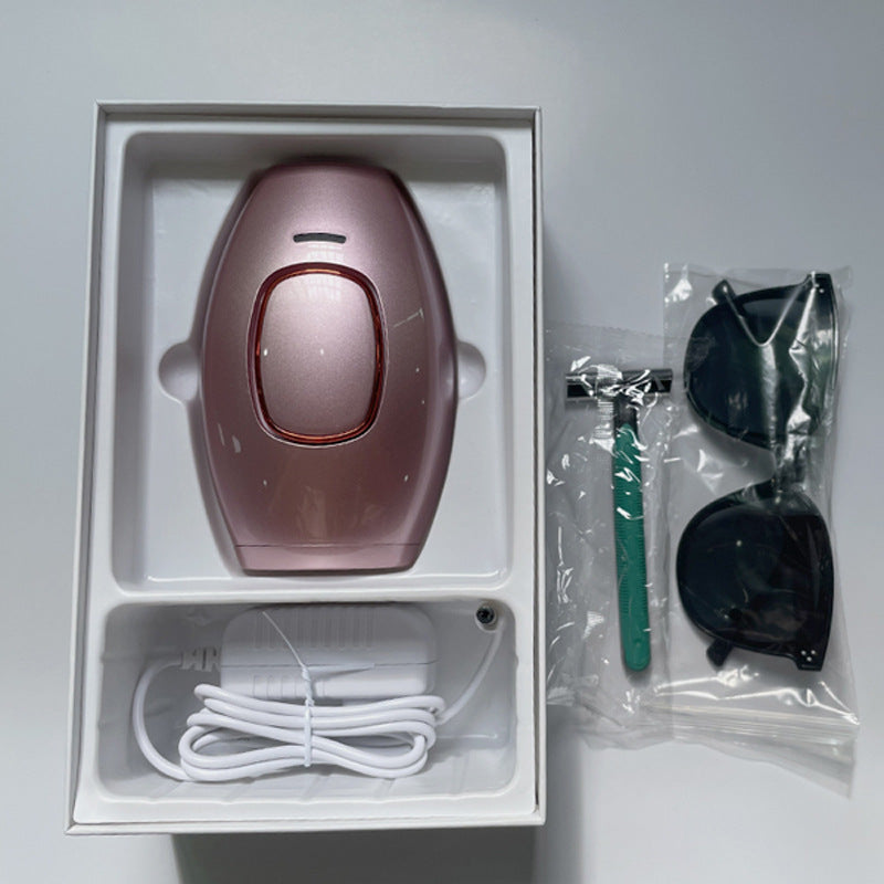 Pink femboy IPL hair removal device displayed inside its packaging alongside USB charging cable, protective goggles, and razor, shown in a neatly organised unboxing layout on a white background