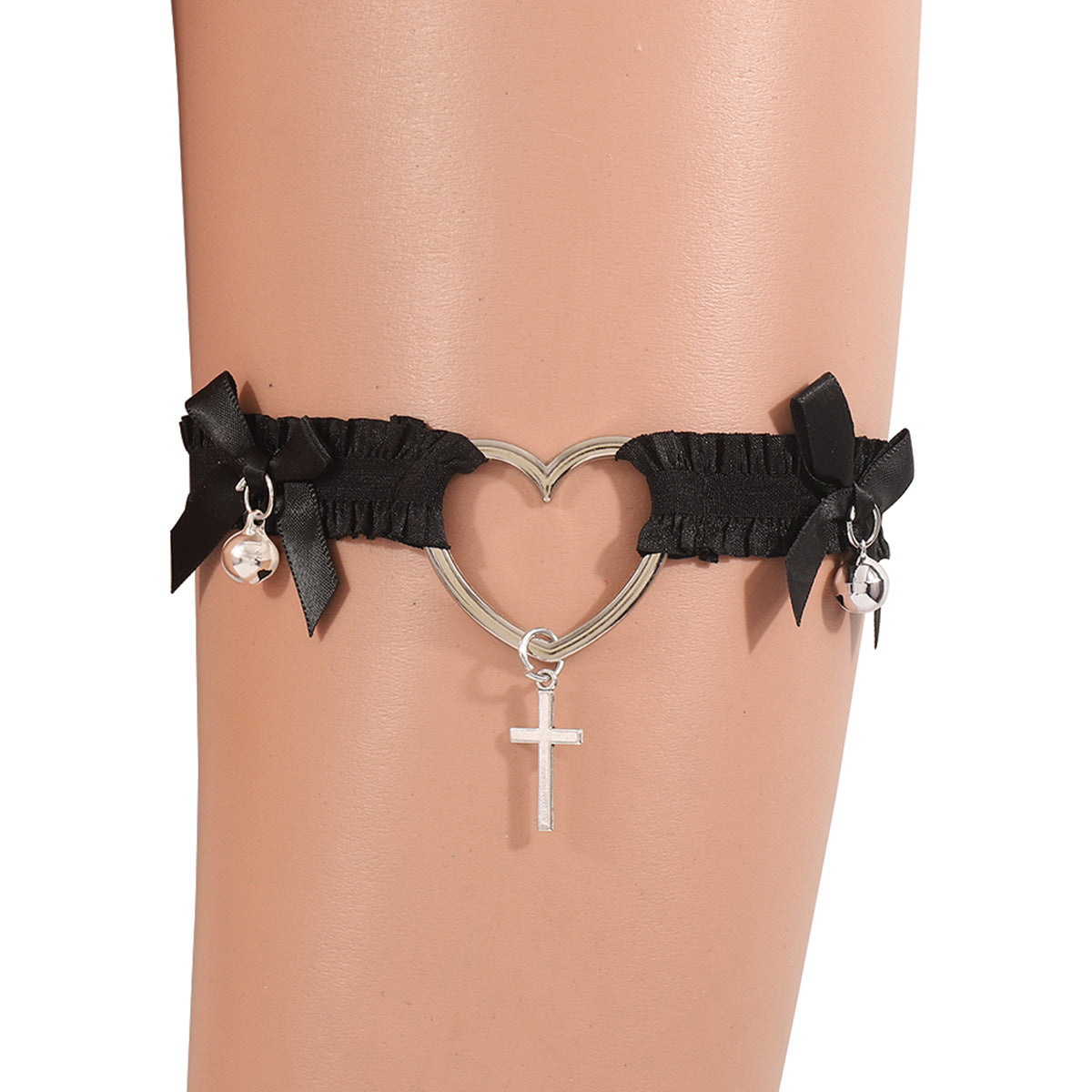 Black heart cross femboy leg garter worn on thigh, featuring elastic lace bands with black satin bows, silver heart-shaped metal ring centerpiece, dangling silver cross charm, and small bell accents, photographed in a close-up studio shot on a mannequin leg, showcasing gothic femboy fashion and femboy accessories.