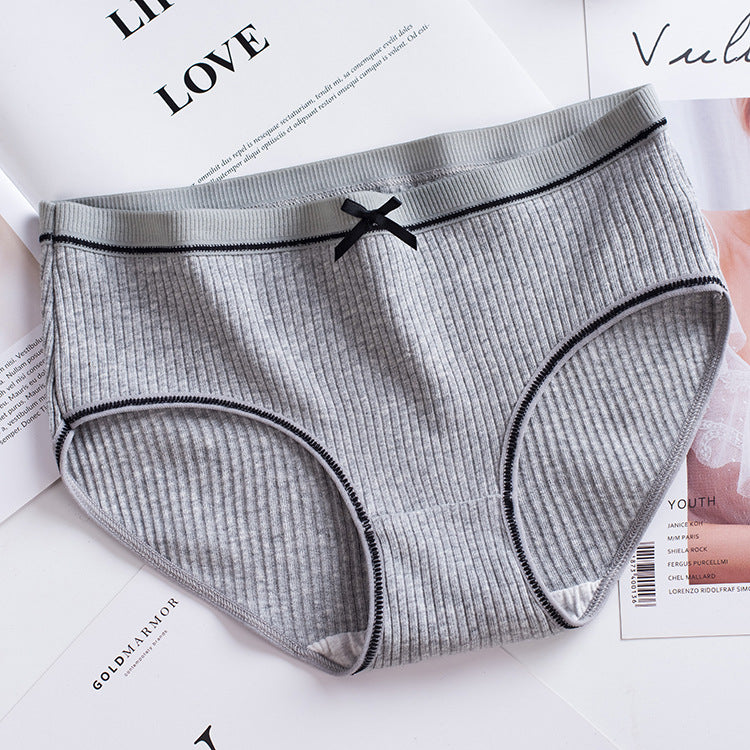 flat-front shot of a single grey ribbed brief with lace trim and small bow detail laid on a white magazine backdrop, showcasing femboy underwear essentials.