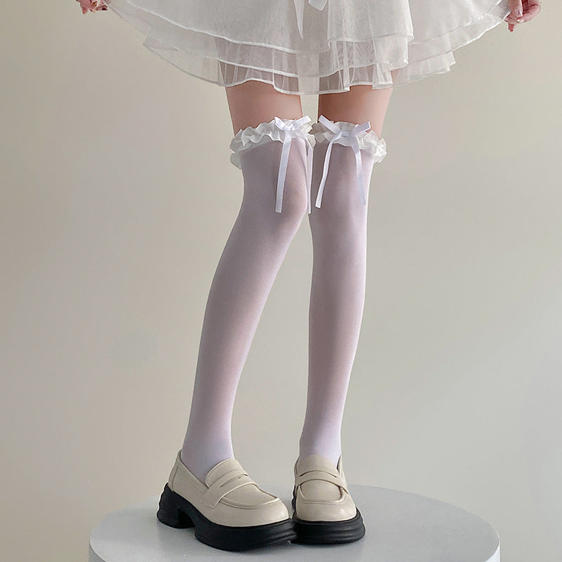 Medium shot of white Bowknot Lolita Thigh Highs with delicate lace trim and bow detailing, styled with cream loafers. Captured in a light, minimalist indoor setting to emphasise femboy clothes and femboy fashion aesthetics.