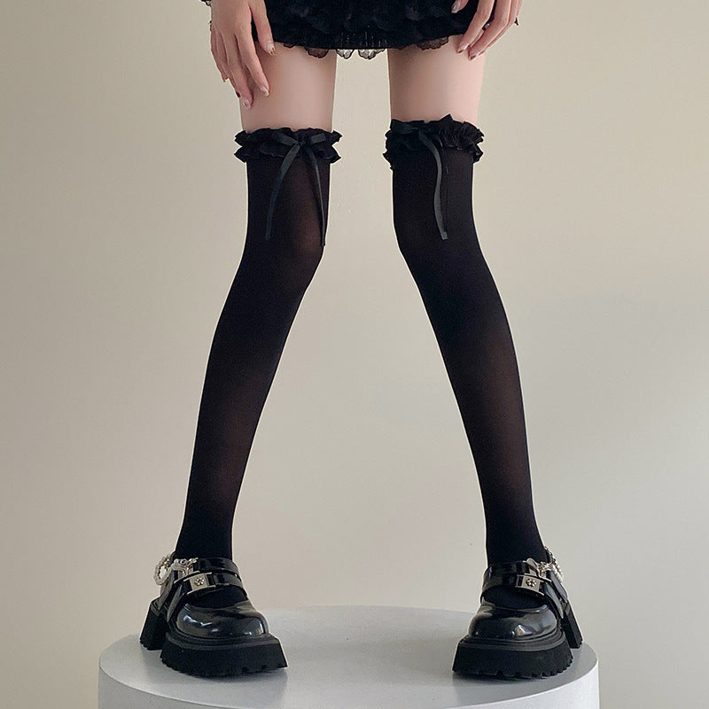 Front view of black Bowknot Lolita Thigh Highs featuring ruffled lace edges and elegant bowknot accents, paired with black chunky platform shoes. Highlighting femboy outfits in a minimalist indoor background.