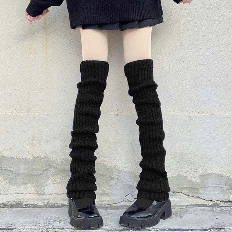 Black knitted leg warmers worn in a stacked oversized style with a pleated skirt and chunky platform shoes, edgy femboy outfit styling.