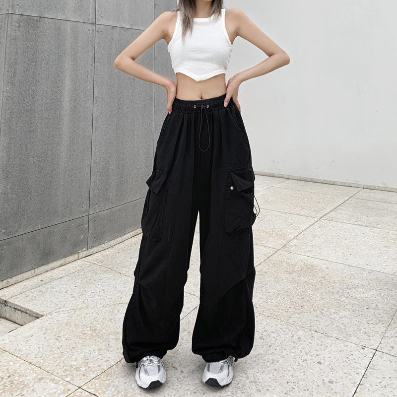 Front view of black high-waisted cargo pants styled with a white cropped tank top, highlighting the utility-inspired design and loose fit, photographed in outdoor lighting – femboy outfits, unisex cargo pants, modern fashion style.