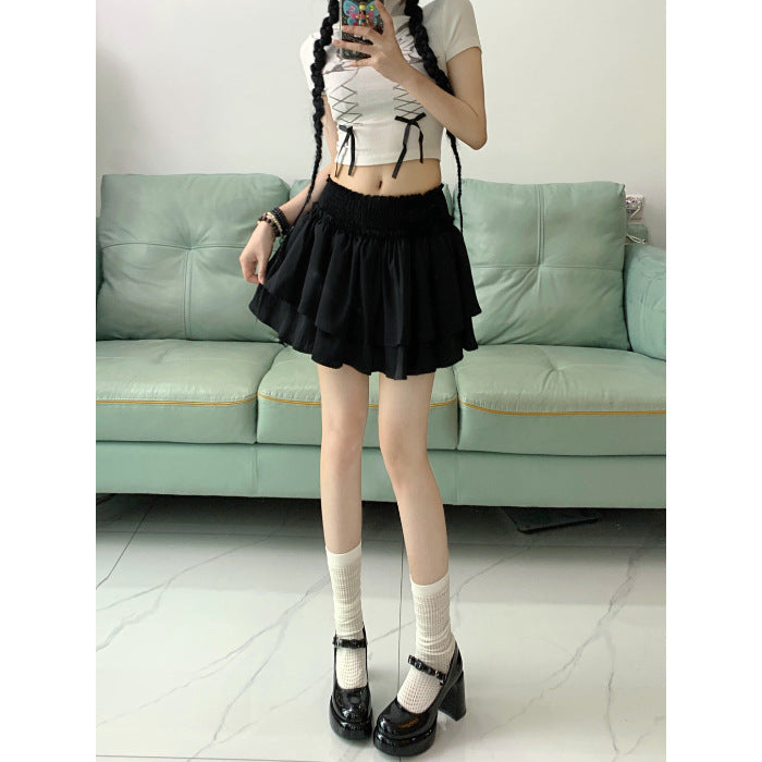 A full-body shot of a model wearing a black ruffle skirt and a white crop top, standing in a modern indoor setting. The layered design of the skirt adds volume and movement, paired with white socks and black shoes, creating a chic and playful femboy outfit. Ideal for fans of femboy fashion and femboy clothing.