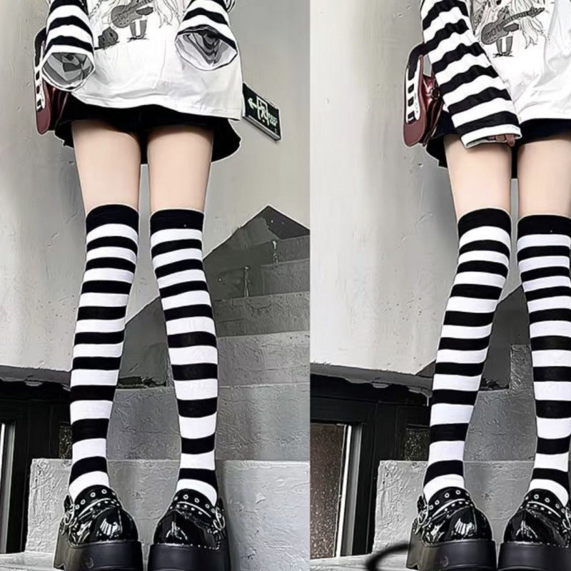Black and white striped thigh high socks worn outdoors on model, casual street-style outfit with platform shoes, long leg emphasis, bold striped pattern, femboy fashion aesthetic.