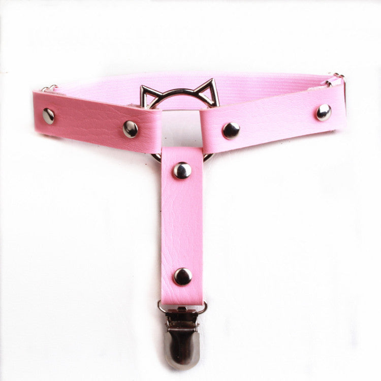 Top-down studio product shot of the pink Cat Face Femboy Thigh Garter photographed from an overhead angle on a clean white background, featuring pastel pink faux leather straps, silver rivets, adjustable elastic band, and a metal cat face ring, a cute femboy thigh garter accessory for pastel femboy outfit aesthetics.