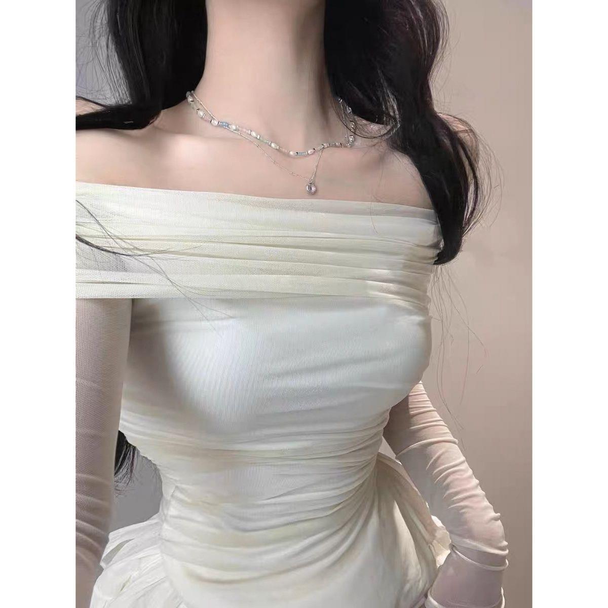 Close-up view of the Chic Femboy Kit featuring an off-shoulder ruched white top with long mesh sleeves and pearl necklace details. Captured indoors with soft lighting, highlighting elegant femboy fashion and style.