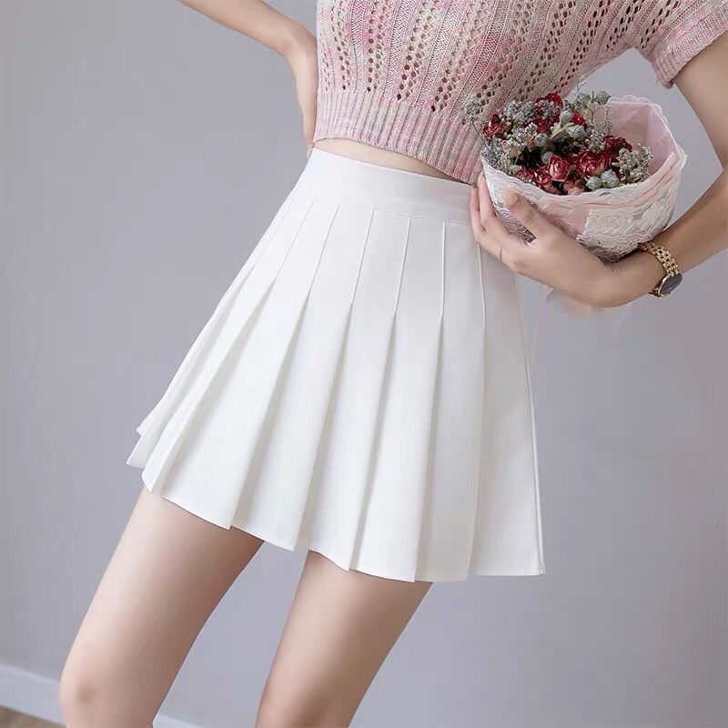 A medium shot of a white pleated skirt held by the model, paired with a light pink top. The clean white background makes the outfit stand out, ideal for femboy outfits with a soft, feminine touch.