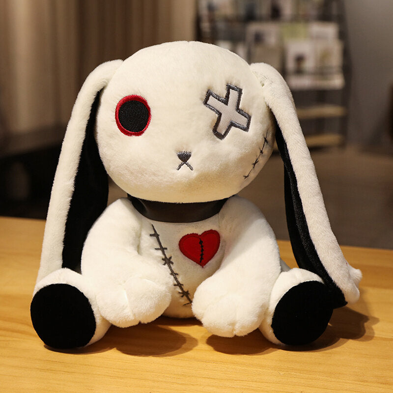 White Dark Bunny plushie sitting upright on a wooden surface, centered front-facing product image featuring stitched heart detail, cross eye embroidery, long floppy ears with black accents, soft gothic bunny plush with cute alternative aesthetic.