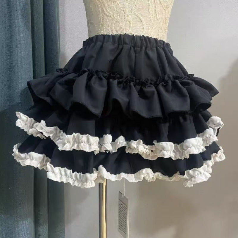 Front view of a dark punk tiered femboy skirt featuring black layered ruffles with white frill accents, shown on a mannequin in an indoor studio setting, highlighting gothic-inspired femboy clothing.
