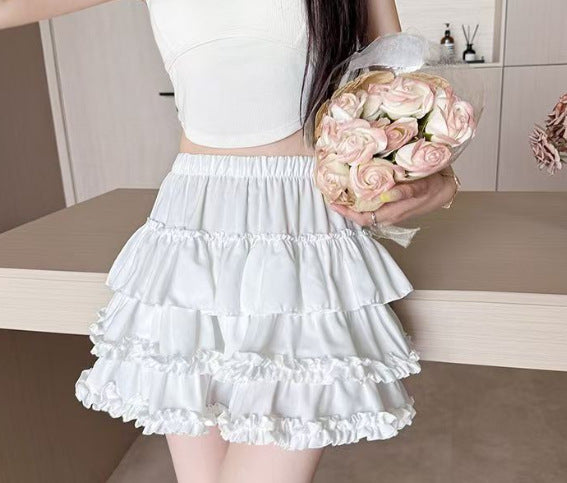 White ruffled tiered femboy skirt worn high-waisted, featuring layered frills and a soft punk-lolita aesthetic, front view mid-shot on model holding flowers, feminine femboy clothing styled for soft goth and punk outfits.