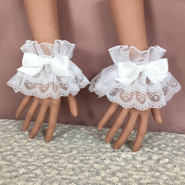 A close-up of a pair of white lace bow bracelets with delicate frills, laying on mannequin hands against a light pink background. The lacework and soft white bows offer a touch of elegance and femininity, ideal for completing femboy outfits or femboy fashion looks.