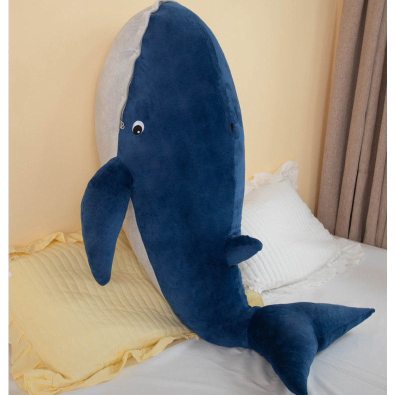 Straight-on lifestyle shot of the oversized Femboy BLÅVINGAD whale plush standing upright on a bed, captured at eye level with warm indoor lighting and neutral pastel bedding, highlighting its large scale and soft finish, styled for cozy femboy room aesthetics from a femboy shop.