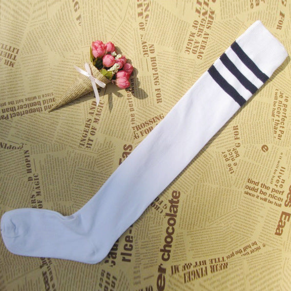 Close-up shot of white thigh-high socks with black stripes at the top, laid flat on a background with vintage newspaper prints and decorative flowers. This charming setup highlights the playful and nostalgic elements of femboy outfits, showcasing a soft and casual approach to femboy clothing.