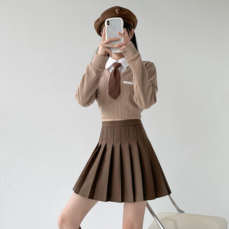 Full-body shot of a model wearing a Biege pleated skirt paired with a matching sweater and tie. The outfit is inspired by school uniforms and offers a refined look for femboy fashion. This school-inspired piece is an essential part of any femboy clothing collection, perfect for creating stylish femboy outfits.