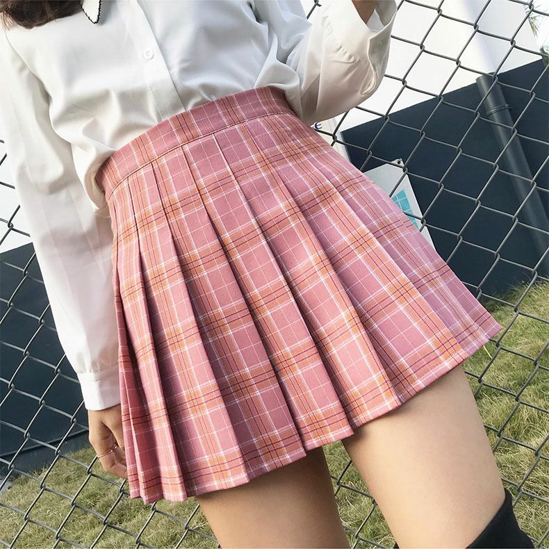 Chic pink plaid pleated skirt showcased on a young model standing by a fence, perfectly blending with femboy fashion for a youthful and fresh look.