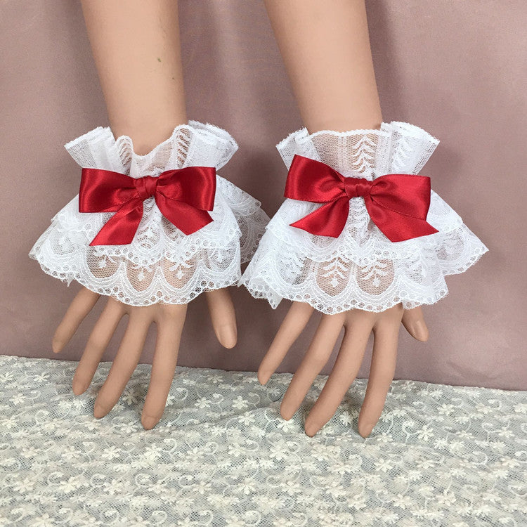 A detailed shot of a pair of lace bracelets featuring vibrant red bows on white lace with intricate patterns, displayed on mannequin hands. These decorative accessories bring a bold statement to any femboy clothing ensemble, blending soft textures with striking colors.