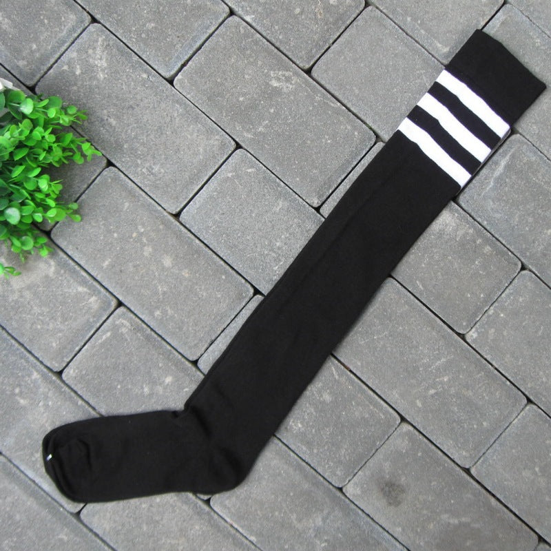 op-down shot of black thigh-high socks with white stripes at the top, placed on a grey brick-textured background with a small green plant as decoration. This minimalistic composition highlights the bold and stylish elements of femboy clothes, perfect for a chic and casual femboy outfit.