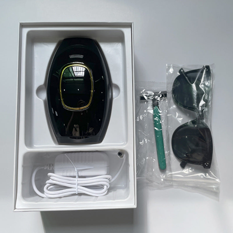 Black femboy IPL hair removal device presented in its retail box with included safety goggles, razor, and charging cable, photographed from a top-down angle on a clean white surface