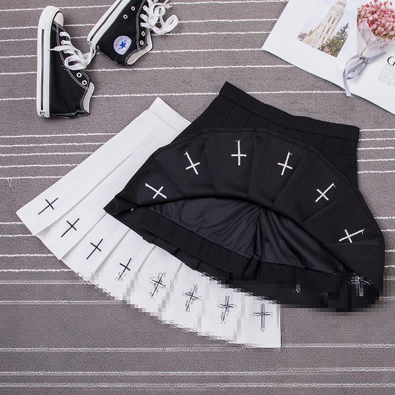 Laid-out Gothic Cross Pleated Skirt featuring white crosses on a black background next to a sneaker and decorative items.