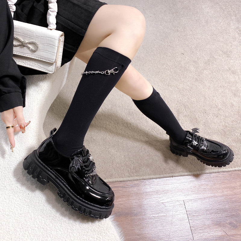 Glossy black Gothic Lolita School Pumps held to display the wing and chain details. These stylish shoes are perfect for anyone looking to express a femboy style with a gothic lolita touch.