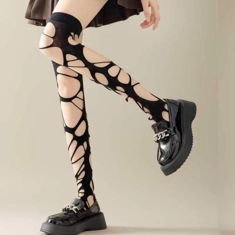 Black gothic ripped fishnet tights with distressed punk cutout details, edgy femboy clothing aesthetic, styled with knee-high boots, studio fashion pose