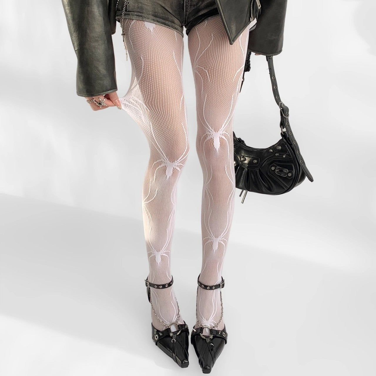 close-up side-angle shot of a model’s legs in white spider-print mesh pantyhose under cuffed gray trousers, styled with black ankle boots on a white backdrop, ideal for chic femboy clothing inspiration.