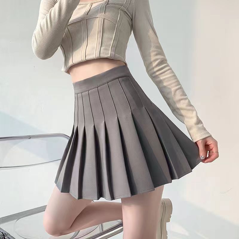 A close-up shot of a model wearing a high-waist gray pleated skirt paired with a ribbed long-sleeve top, set against a soft indoor backdrop. The skirt's clean pleats add structure to the outfit, perfect for creating chic femboy outfits and enhancing your femboy fashion look.