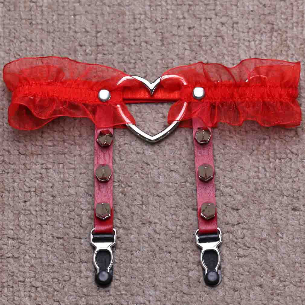 Flat lay product shot of the red Heart Lace Femboy Garter photographed from a top-down angle on a neutral textured background, featuring sheer red lace trim, adjustable straps, silver heart hardware, and metal clips, a cute and sexy femboy accessory designed to style femboy skirt and femboy outfit aesthetics.