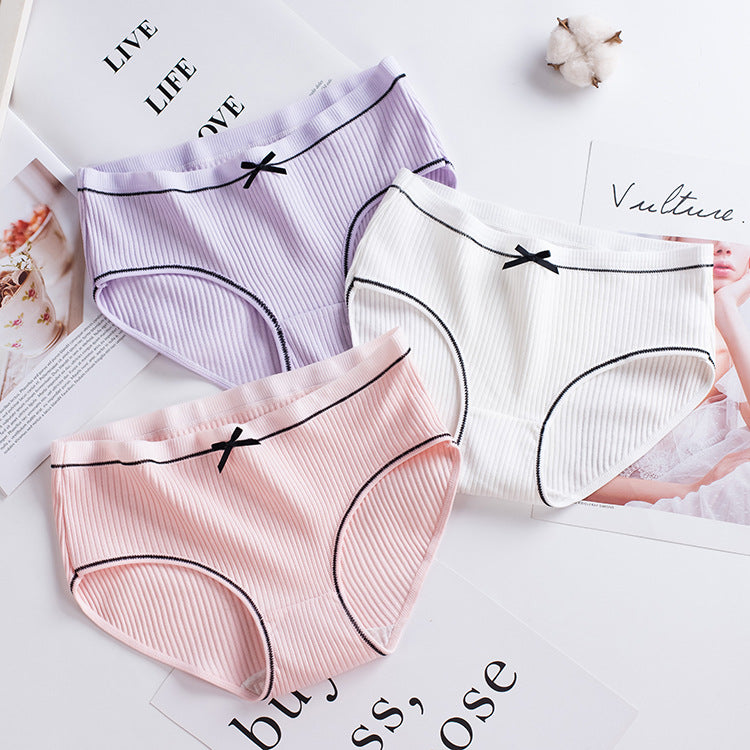 overhead shot of three ribbed briefs in lilac, pink, and white arranged neatly on a white tabletop with cotton accents, highlighting soft pastel femboy briefs.

