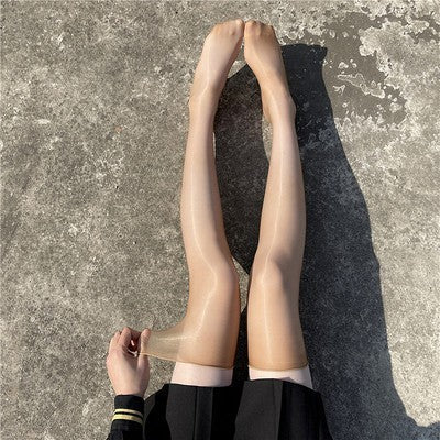 A close-up of nude glossy thigh-high stockings worn by a model sitting on a concrete surface in sunlight. The sheer, shiny finish enhances the legs, making these thigh-highs perfect for adding a sleek and elegant touch to femboy outfits.