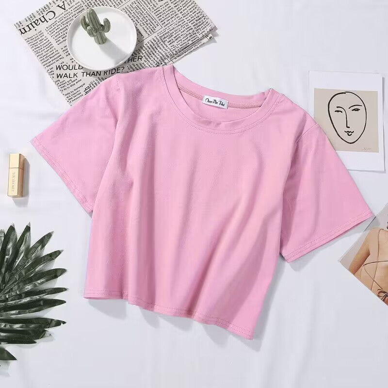 A flat lay of a pink Loose Crop Top Tee placed on a white surface, styled with a minimalist background. This casual tee is perfect for creating femboy outfits and pairing with high-waisted shorts or skirts.