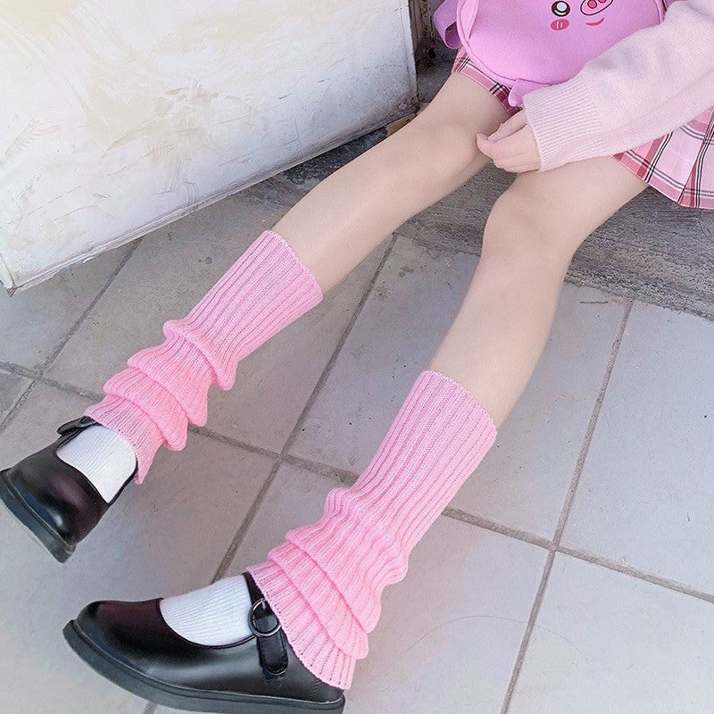 Pink knitted leg warmers matched with loafers and pastel outfit, lower-body angled shot, soft daylight tones, cute pastel femboy fashion look.