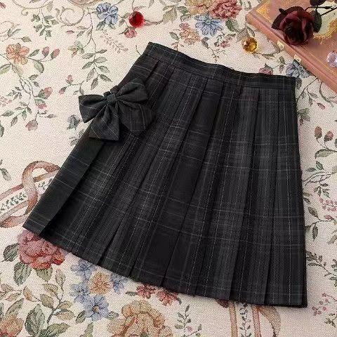 Flat lay of a plaid pleated skirt with a bow detail, part of the Femboy Schoolgirl Kit. Perfect for achieving a classic schoolgirl look in femboy fashion.