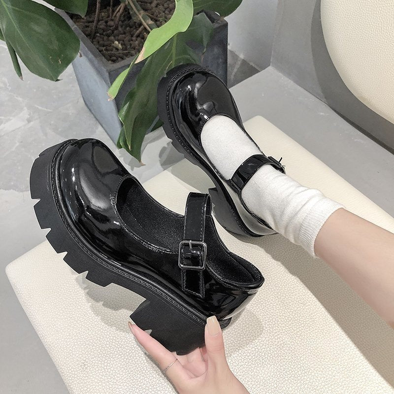 Black glossy school pumps held indoors with a focus on their sturdy chunky heels. A versatile choice for femboy fashion and everyday wear.