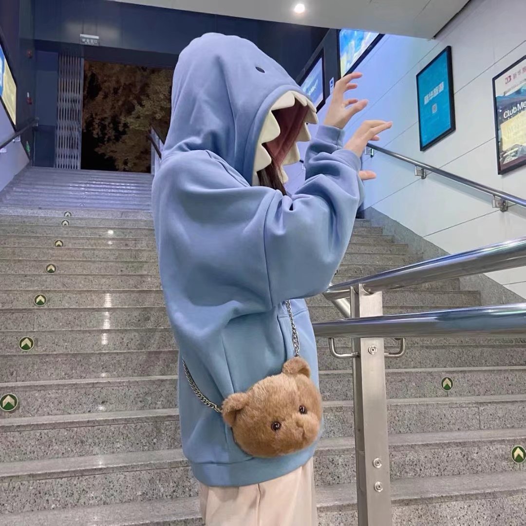 Person in a playful pose wearing a sky blue shark hoodie, highlighting a youthful and fresh style suitable for femboy outfits.