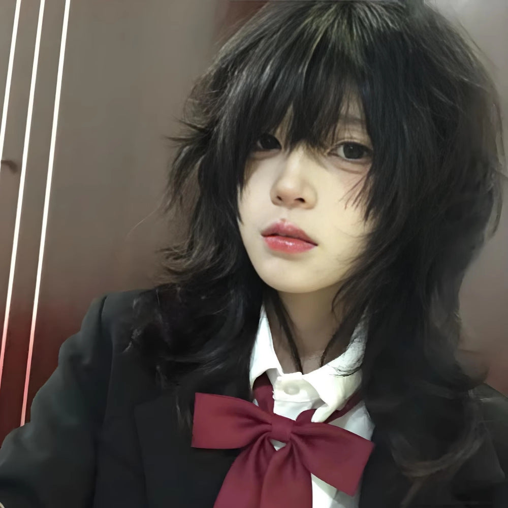 Front-facing portrait shot of a model wearing a soft wave wolf femboy wig in black, featuring layered shaggy texture and long wispy bangs, styled in a Japanese-inspired androgynous femboy fashion look against an indoor background.