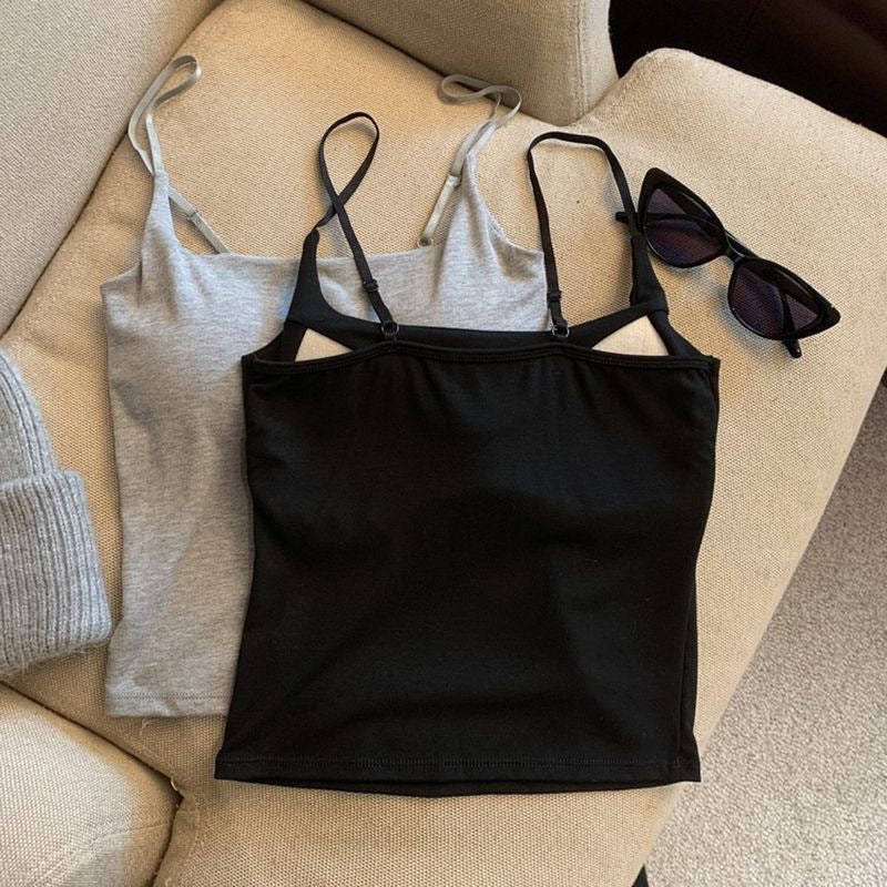 A top-down view of a black camisole placed over a gray one, arranged on a beige couch, paired with black sunglasses. This stylish solid colour camisole is a staple in femboy fashion and femboy outfits.
