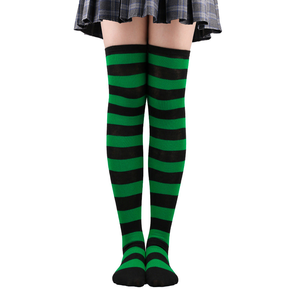Green and black striped femboy thigh high socks worn on legs in a centered studio photograph, soft breathable cotton with elastic fit, vibrant striped style for alternative femboy outfits, photographed on a white background.