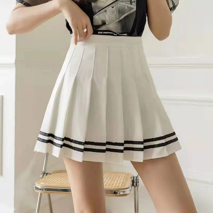 A close-up of a white pleated skirt with black stripes near the hem, styled with a casual black graphic tee. The image captures a mid-shot from waist to thigh, with a clean white background, highlighting femboy clothing in a relaxed setting.