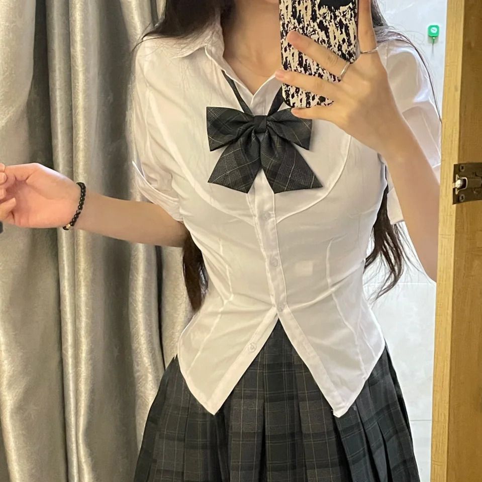 Close-up of a fitted white short sleeve shirt with a plaid bow and pleated skirt, styled as part of the Femboy Schoolgirl Kit. Ideal for adding an academy-inspired touch to femboy outfits.