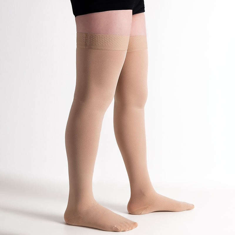 Side angle standing shot of nude thigh-high xtra long femboy stockings, photographed on a clean white backdrop with diffused lighting, emphasizing the snug upper band and smooth compression look for femboy fashion.